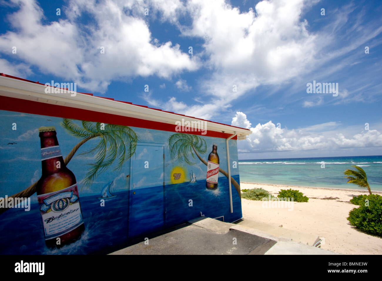 Spiaggia caraibica negozio con Budweiser e roccia di rotolamento birra arte sul lato. Sabbia e mare e acqua in background. Blue Skies nuvole Foto Stock