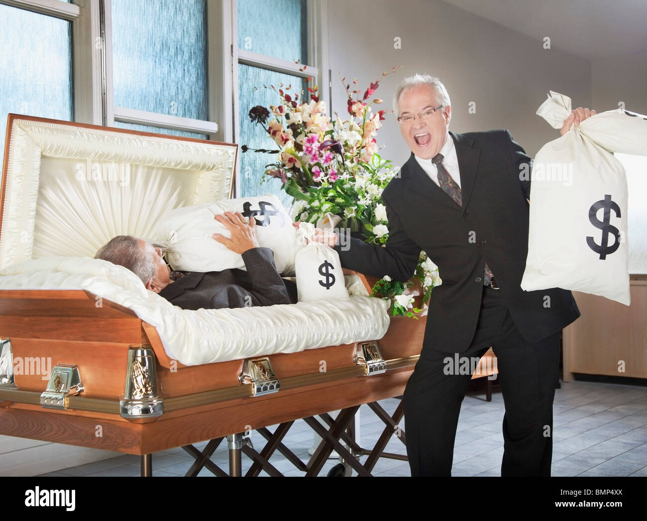 Edmonton, Alberta, Canada; un uomo felice Tiene borse di denaro accanto a un uomo deceduto in una bara Foto Stock