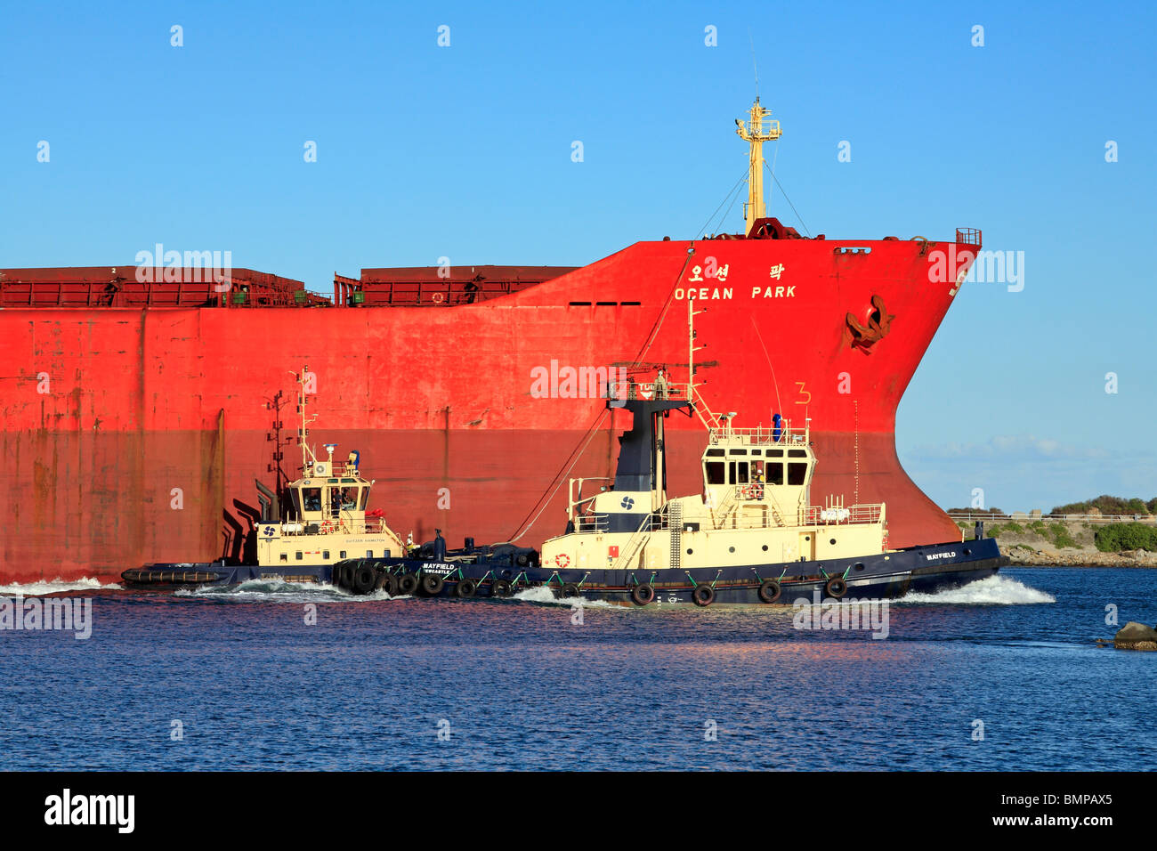 Nave cargo entrando in porto di Newcastle, Australia, accompagnato da due barche rimorchiatore. Foto Stock