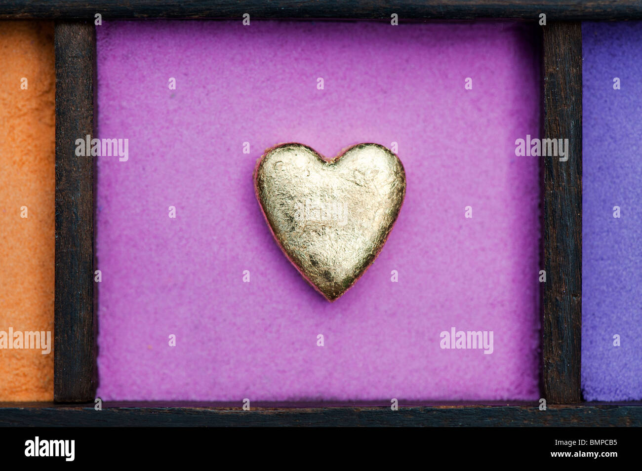 Oro forma di cuore contro la sabbia rosa in un vassoio di legno Foto Stock