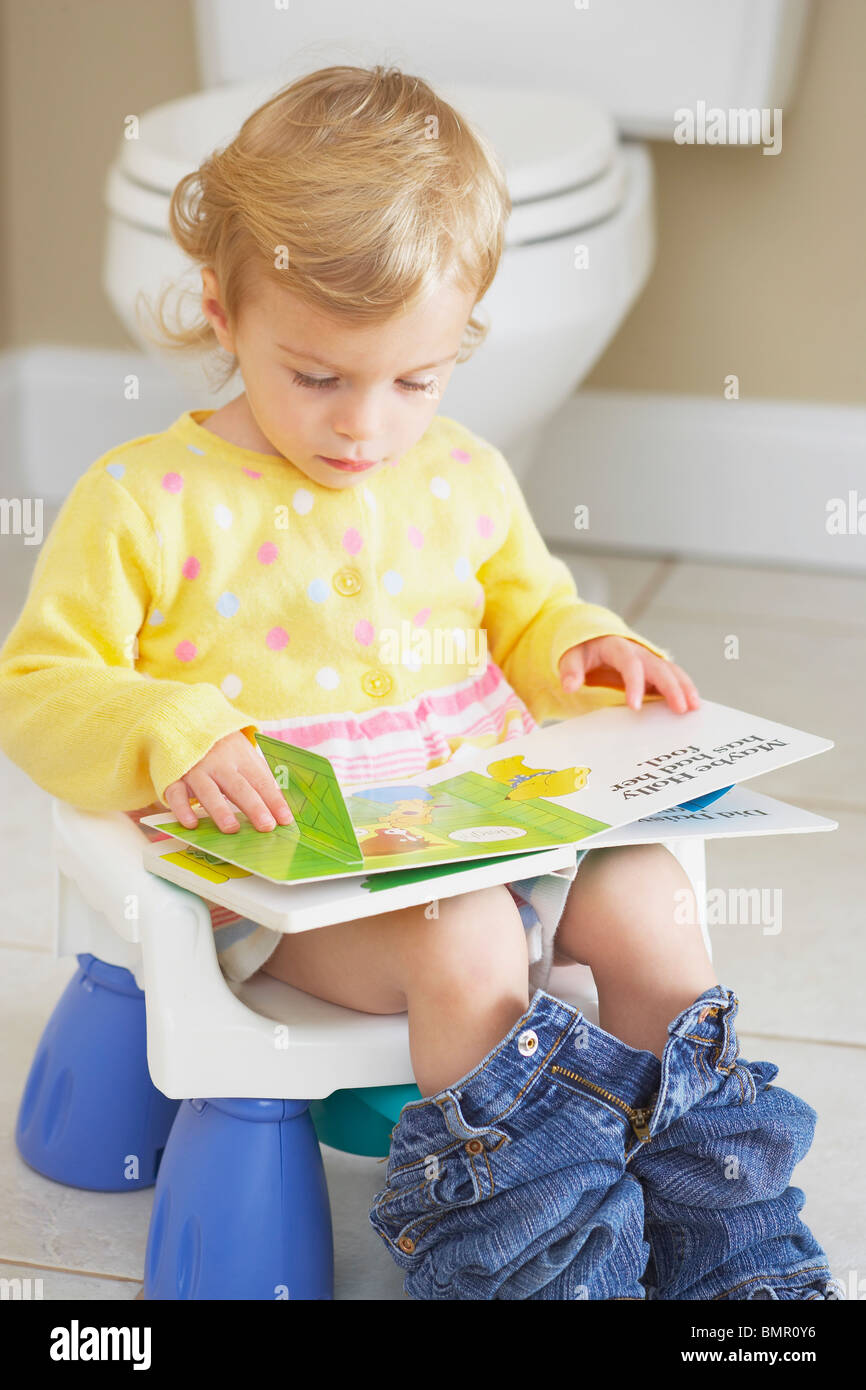 Knoxville, Tennessee, Stati Uniti d'America; un giovane bambino seduto su un seggiolino per bambini. Vasino e la lettura di un libro Foto Stock