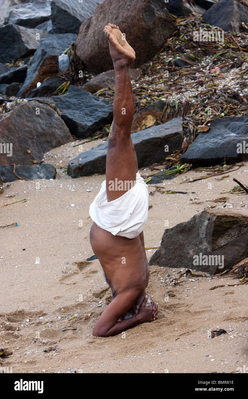 Un yogi eseguire Sirsasana (Headstand) nella spiaggia di Kochi (Cochin), Kerala, India. Foto Stock