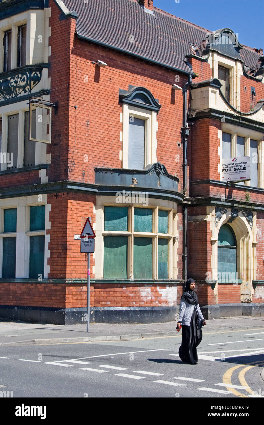 Giovane donna camminare passato intavolato ,chiuso pub (ex Langworthy Hotel), Langworthy Road, Salford, Greater Manchester, Regno Unito Foto Stock