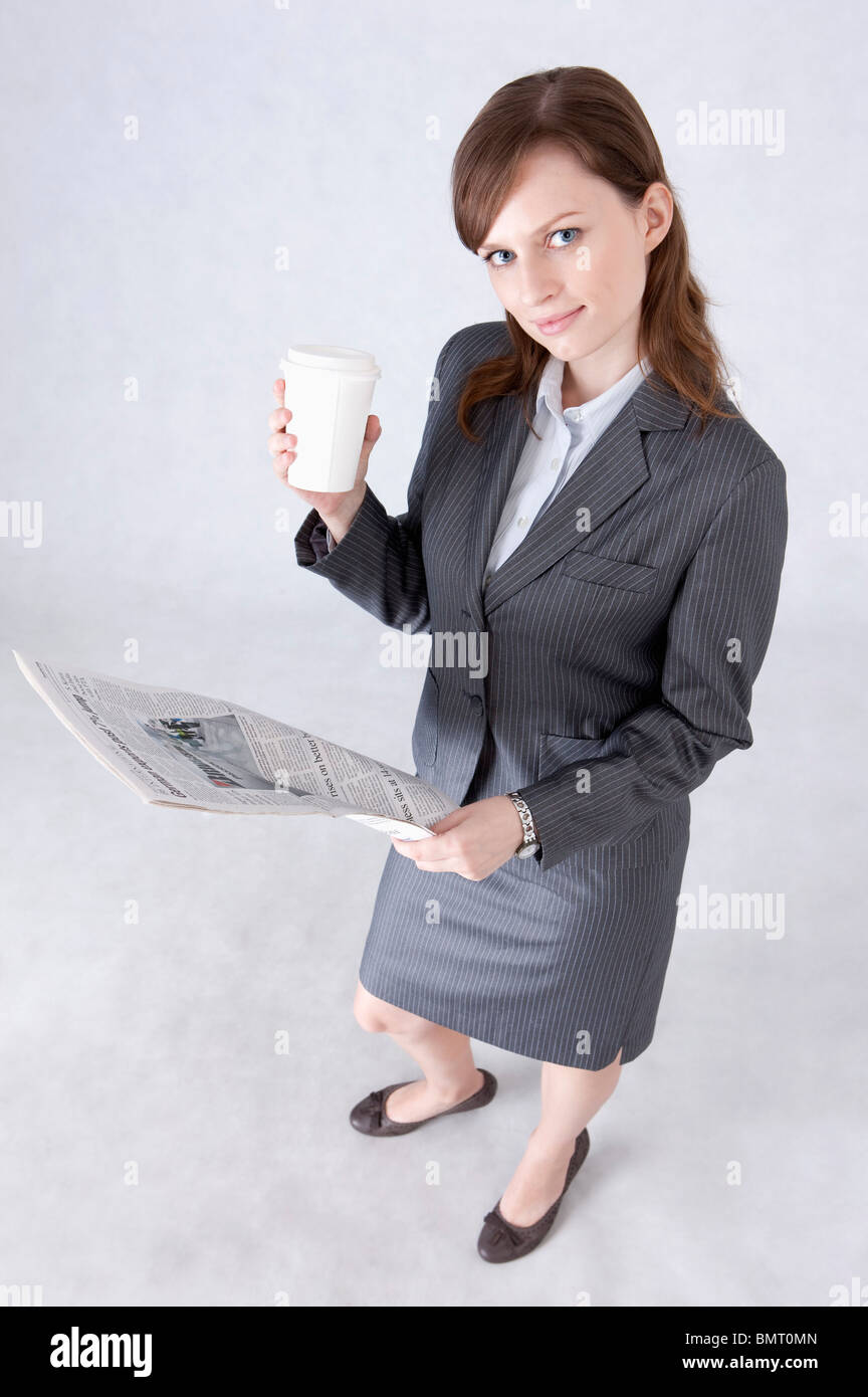 Imprenditrice tenendo una tazza e giornale e guardando in alto Foto Stock
