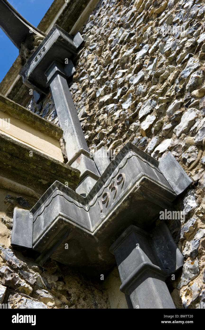 Parte di una derivazione della parte iniziale dello scarico delle acque piovane sulla pietra focaia la parete esterna di una chiesa. Foto Stock