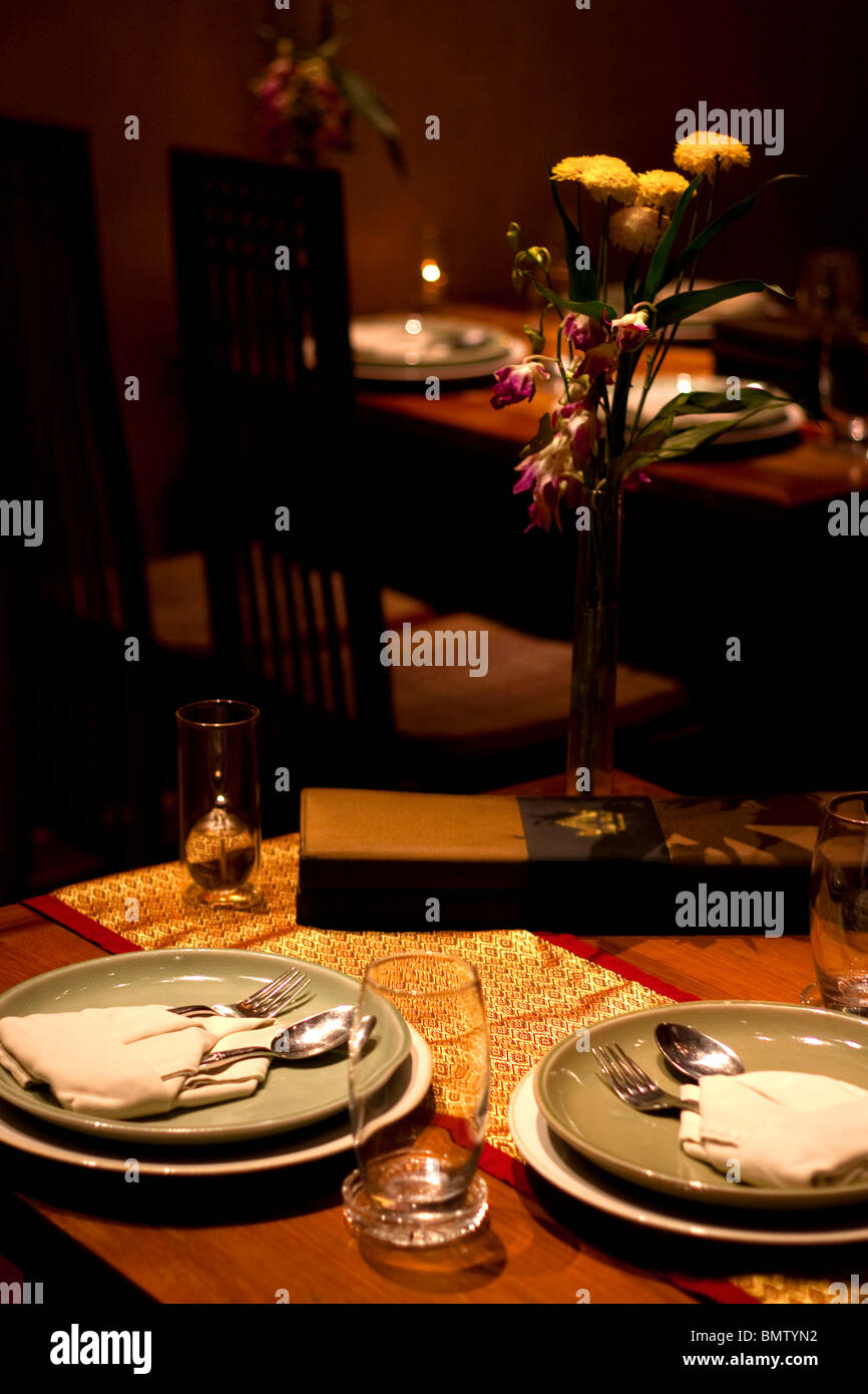 Inserire le impostazioni per due nel ristorante Thai con fiori, candele olio, bicchieri, cucchiaio, forcella e il panno assorbente Foto Stock