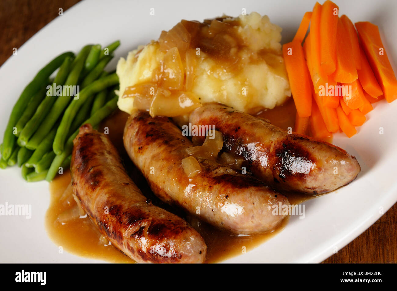 Foto di stock di una piastra di salsicce, purè di patate, fagioli verdi, le carote e la cipolla con sugo di carne. Foto Stock