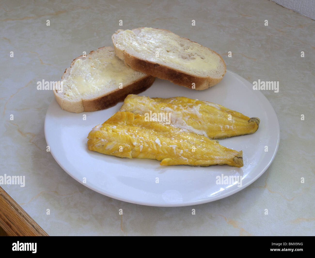 Eglefino affumicato Filetti e bianco imburrato crostini di pane su una piastra per cena Foto Stock