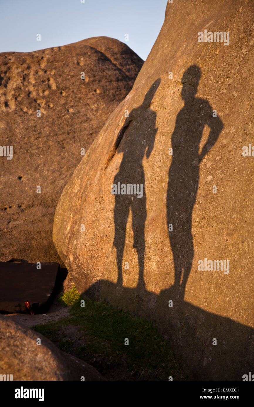 Le ombre dei due alpinisti su un masso in serata calda luce del sole in Burbage inferiore, il Peak District. Foto Stock