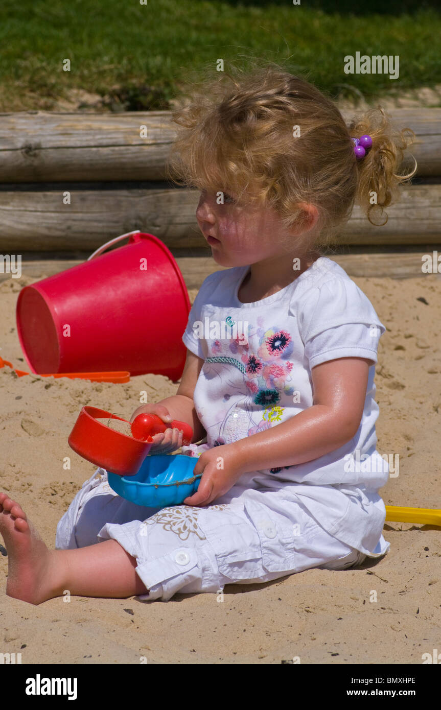2 anno vecchia ragazza giocando in una buca di sabbia con dei giocattoli di plastica Foto Stock