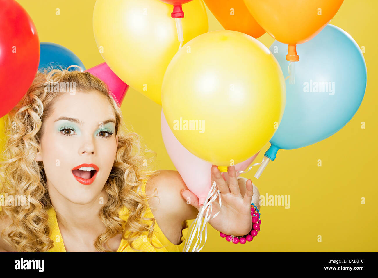 Giovane donna bionda con palloncini contro sfondo giallo Foto Stock