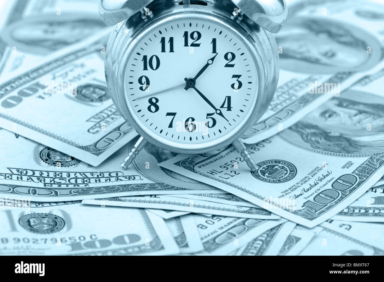 Tempo - denaro. Il concetto di business. Ore analogico su un mucchio di dollari di carta. Le tonalità blu Foto Stock