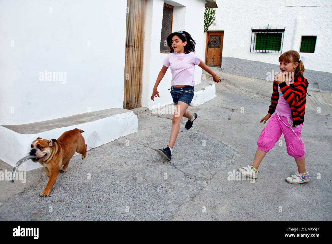Le ragazze in esecuzione dietro un cane con bastone, Capileira, Andalusia, Las Alpujarras, Spagna Foto Stock