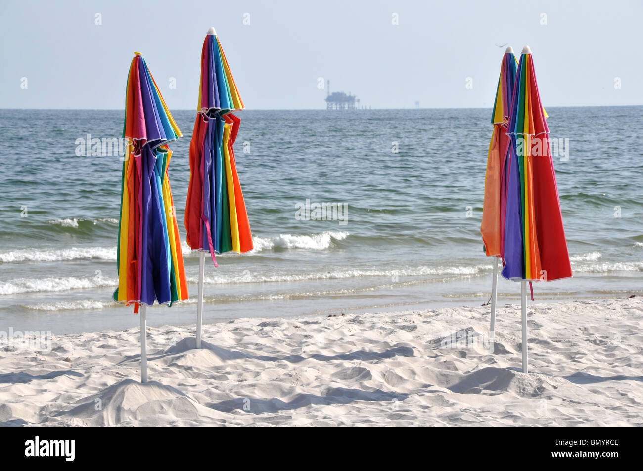 Abbandonata la spiaggia con ombrelloni chiusi. Off shore oil rig in background. Foto Stock