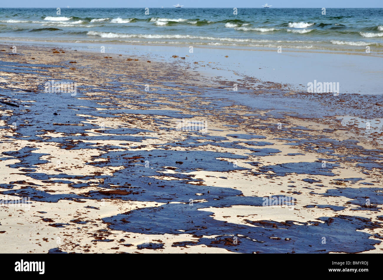 Fuoriuscita di olio sulla spiaggia con olio skimmers in background. Foto Stock