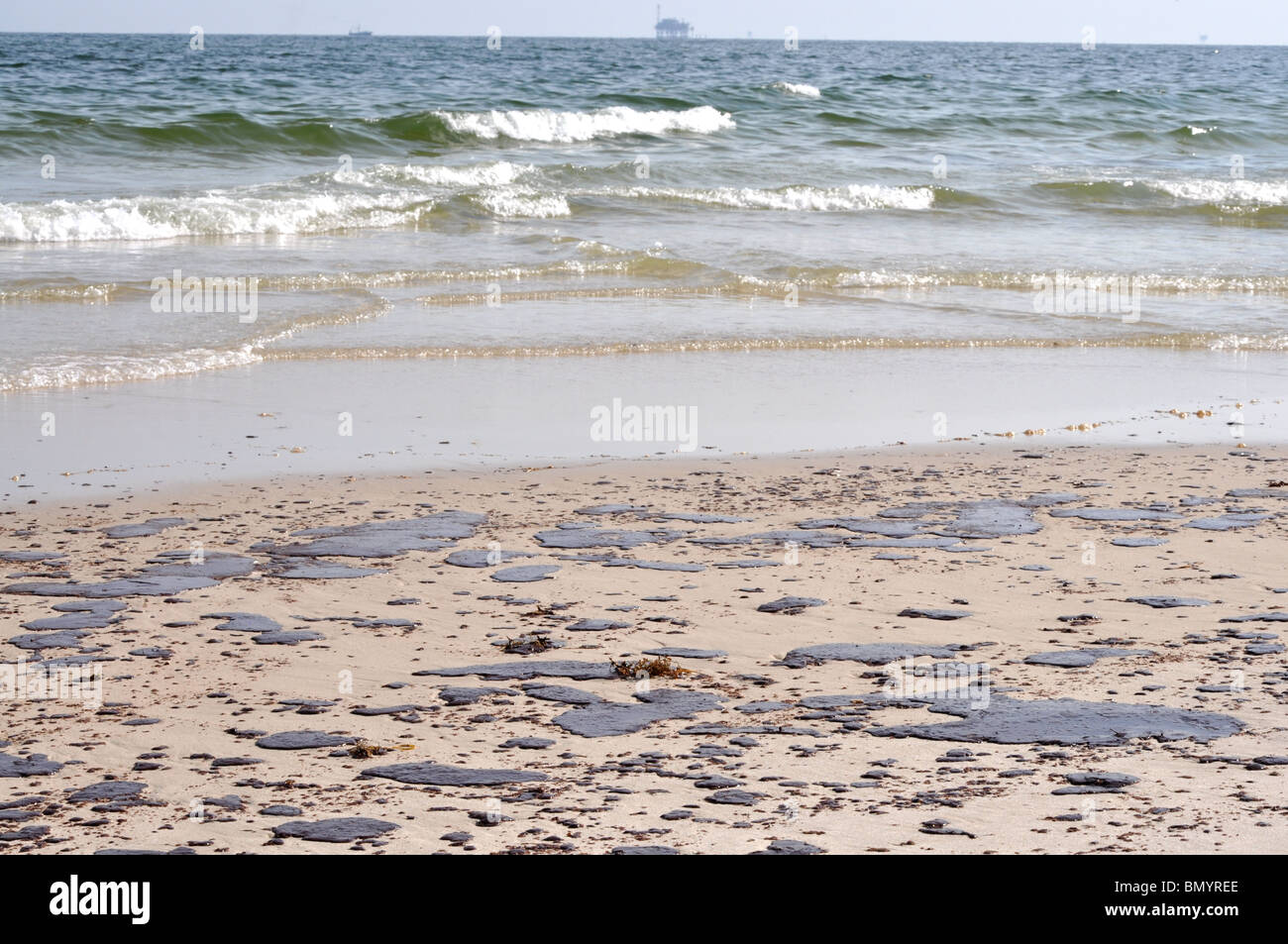 Fuoriuscita di olio sulla spiaggia con off shore oil rig in background. Foto Stock