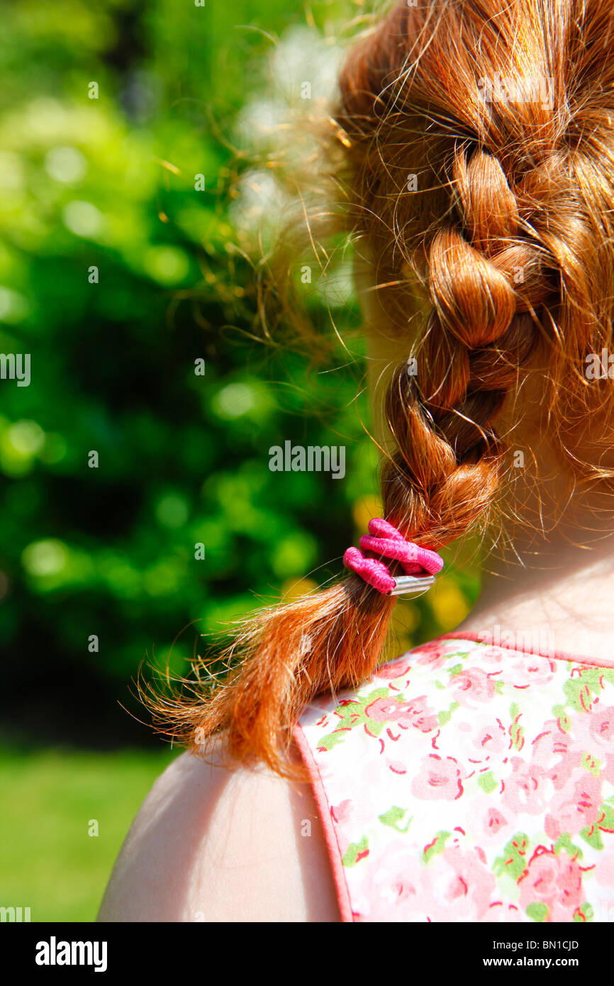 Dai capelli rossi quattro anno vecchia ragazza in un giardino con trecce. Vista da dietro. Foto Stock