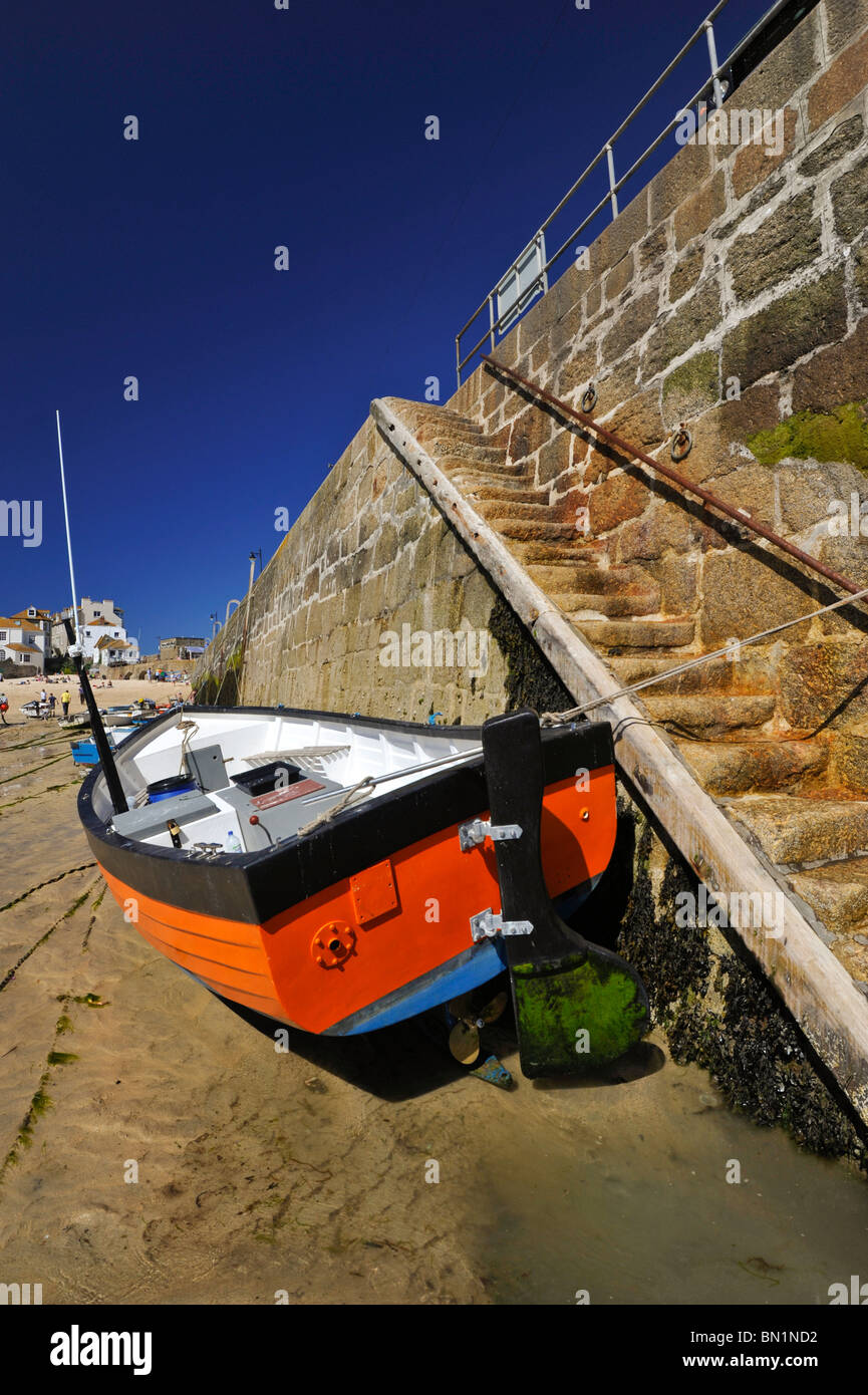 Vivacemente colorato piccola barca da pesca accanto a una banchina in pietra e gradini in St Ives Harbour Cornwall, Regno Unito Foto Stock