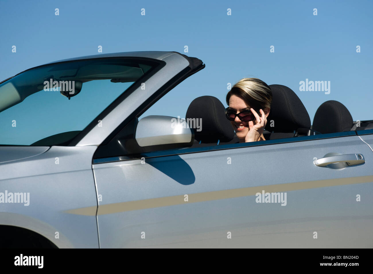 Donna Nel convertibile, abbassando gli occhiali da sole per guardare la fotocamera Foto Stock