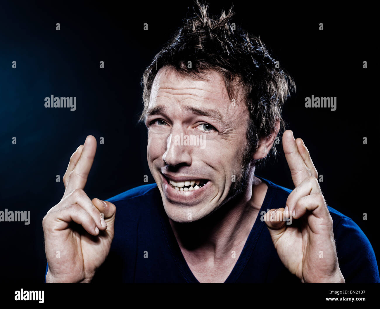 Ritratto in studio su sfondo nero di un divertente espressiva uomo caucasico con dita incrociate sperando fortunati Foto Stock