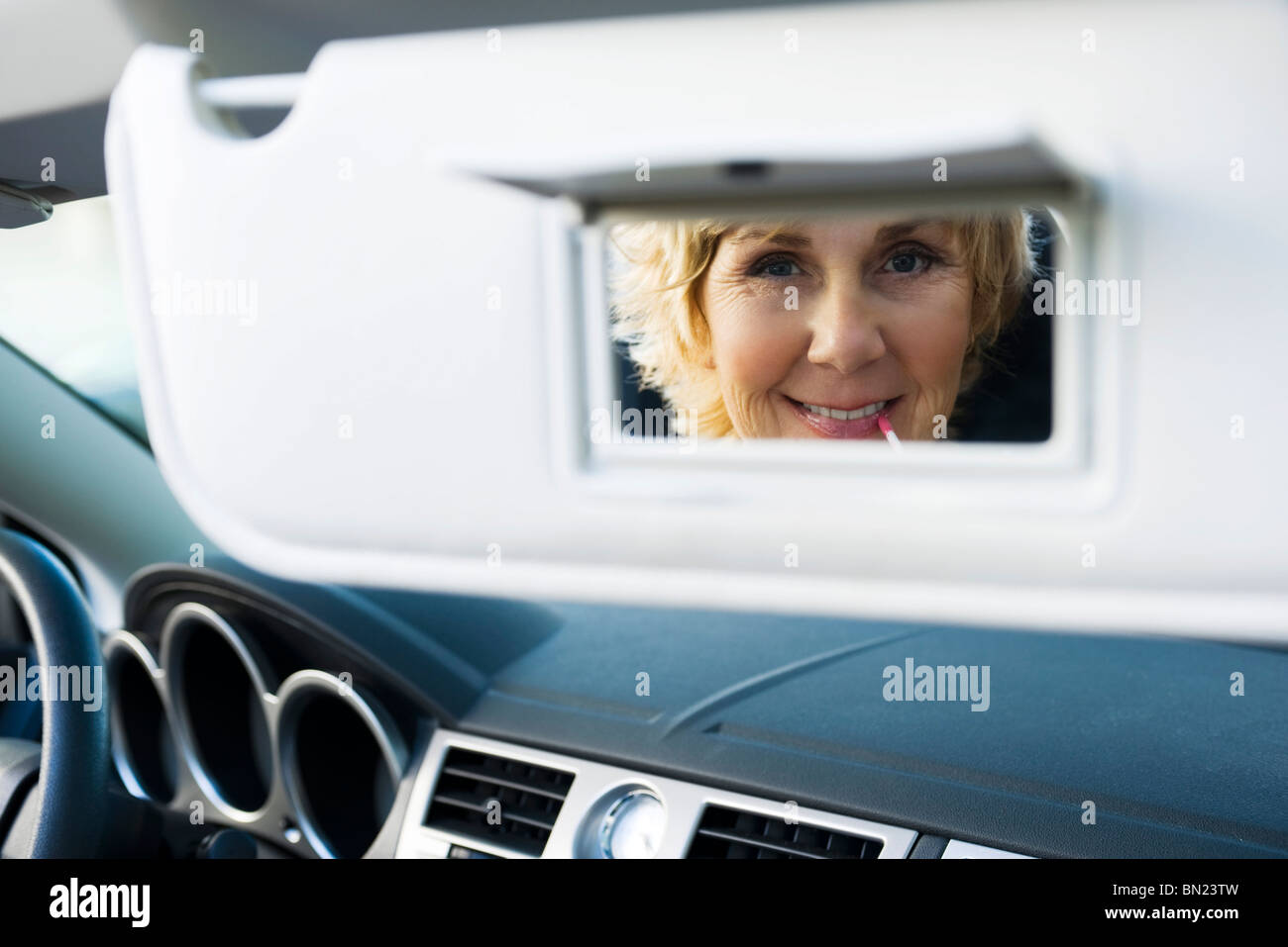 La donna in auto utilizzando la visiera specchietto di cortesia per mettere sul make-up Foto Stock