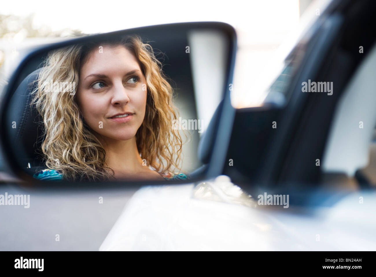 Giovane donna alla guida di auto e la riflessione in vista laterale lo specchio Foto Stock