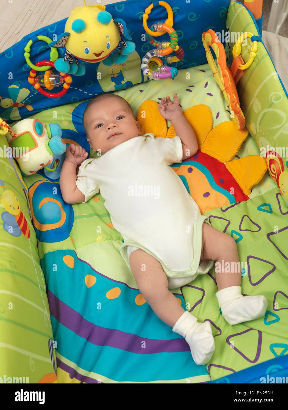 Sei settimane vecchio simpatico bimbo giacente in un colorato tappeto gioco con giocattoli Foto Stock