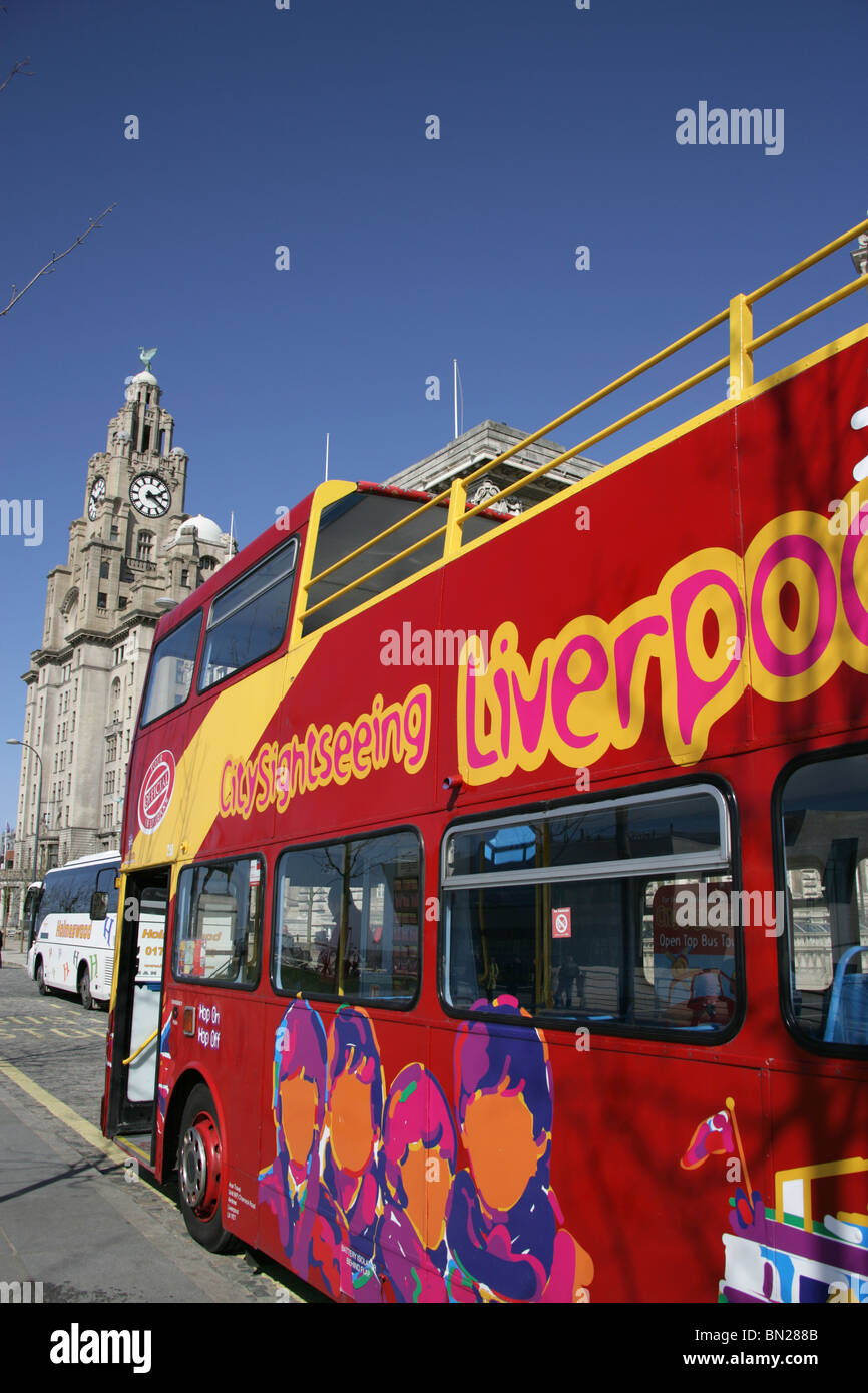 La città di Liverpool, in Inghilterra. Red visitatore tour bus parcheggiato a Pier Head esplanade con il Royal Liver Building in background. Foto Stock