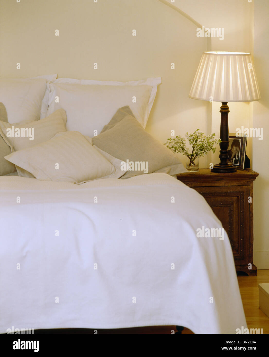 Lampada accesa sul comodino accanto al letto con cuscini color crema e letto bianco-cover Foto Stock