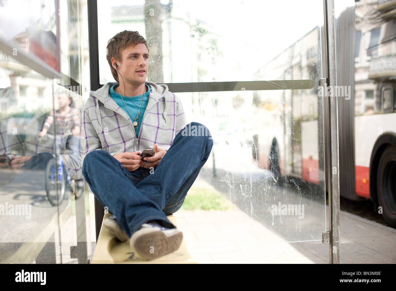 Giovane uomo seduto in una fermata autobus e utilizzando un mp3-player, basso angolo di visione Foto Stock