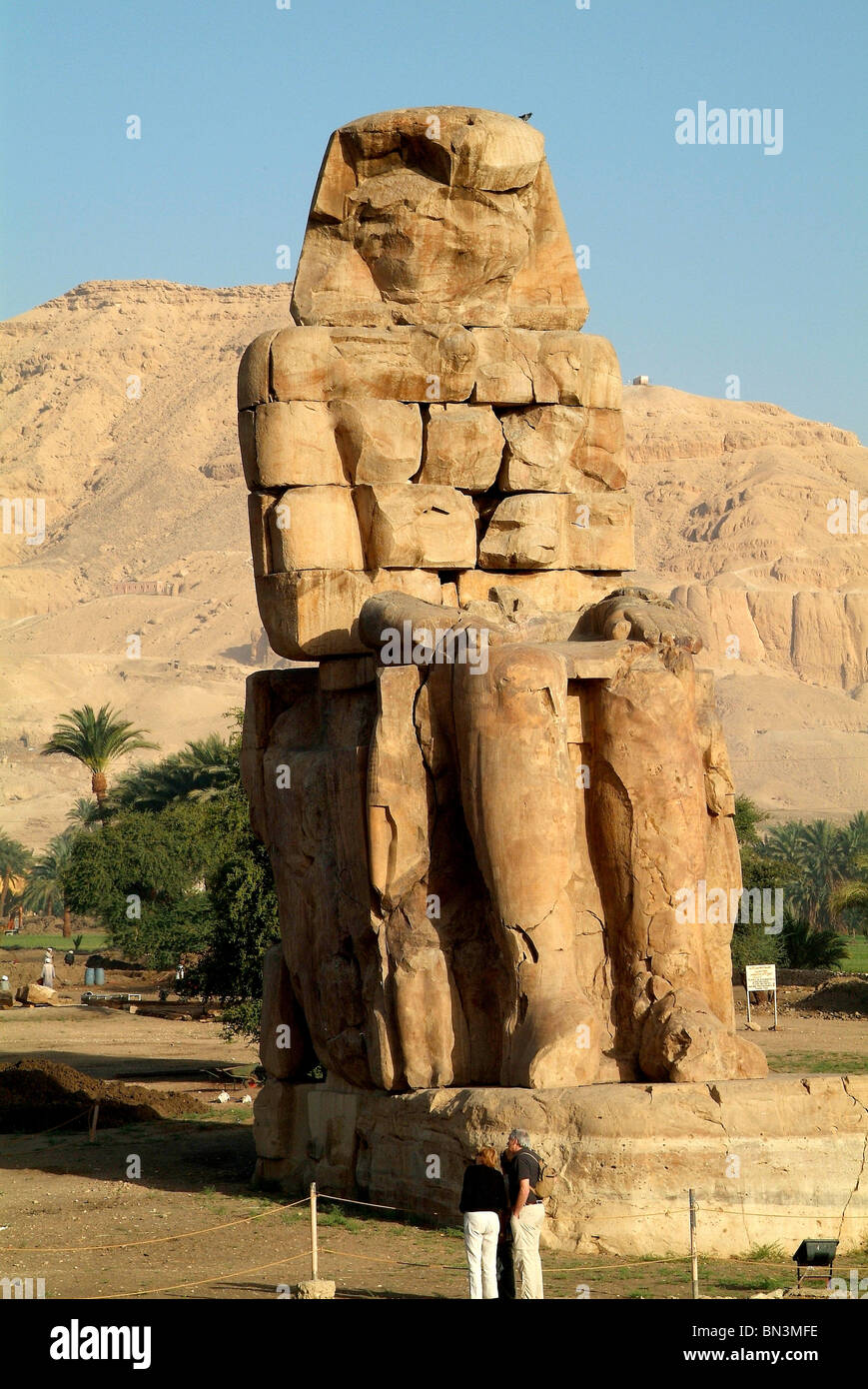 I turisti nella parte anteriore di un Colosso di Memnon, Luxor, Egitto Foto Stock