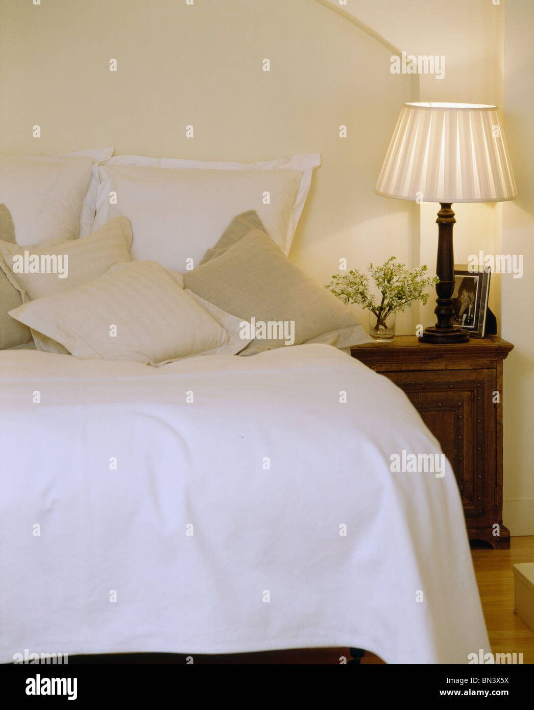 Lampada accesa sul comodino accanto al letto con la crema lenzuola e cuscini letto bianco-cover Foto Stock