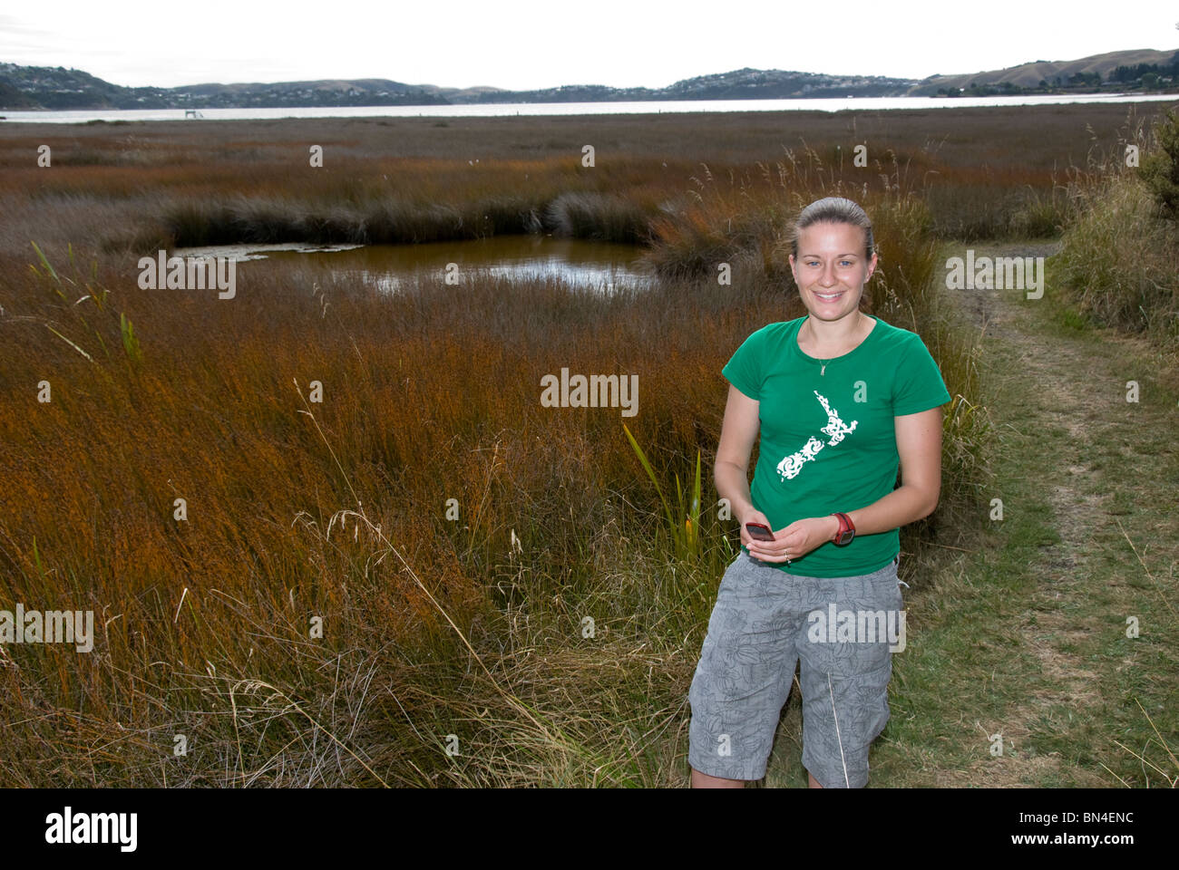 Giovane donna, 20's, in verde Nuova Zelanda tee shirt a riserva faunistica, paludi, Ingresso Pauatahanui, Wellington, Isola del nord, Foto Stock