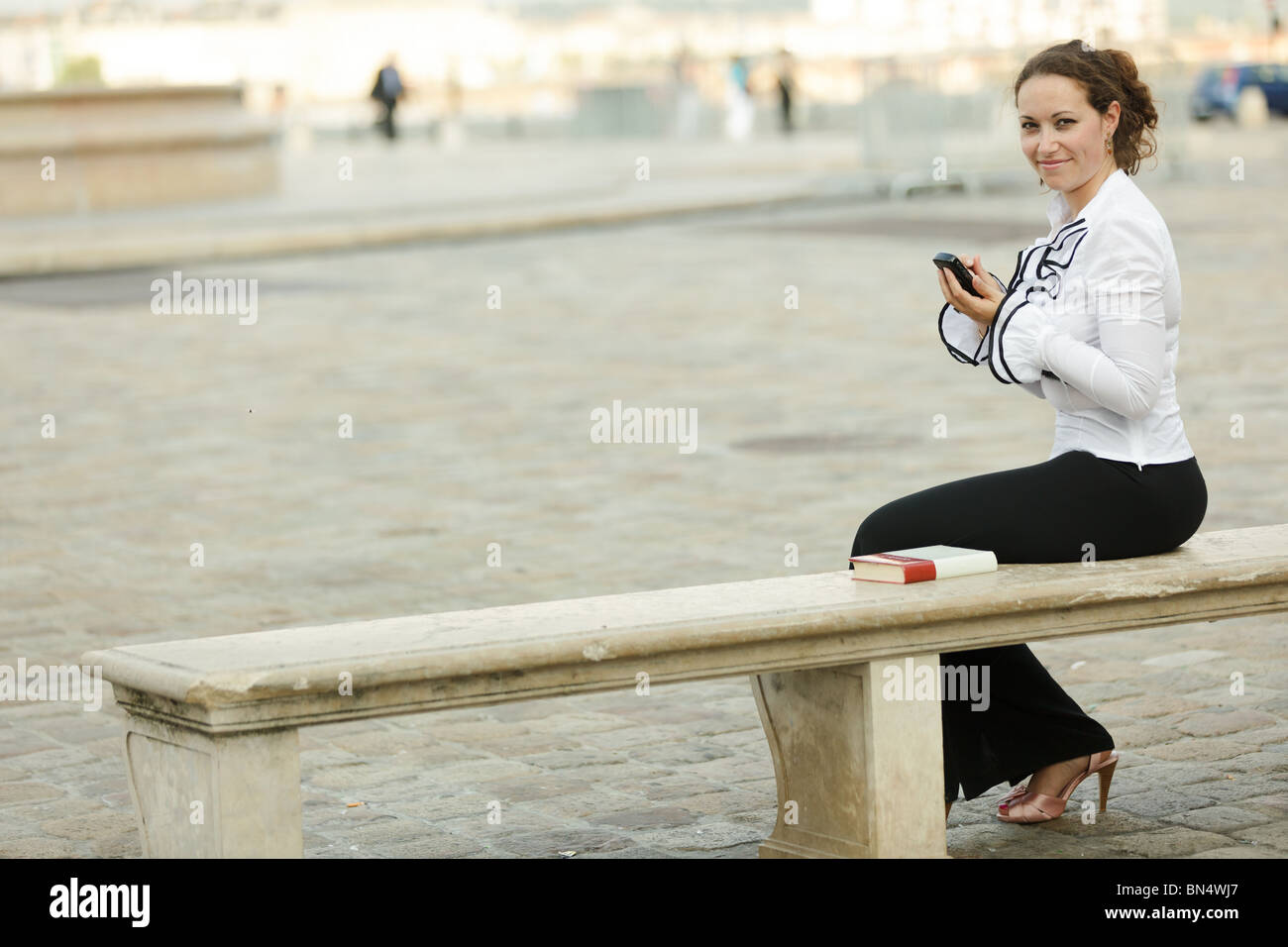 Business donna seduta sul banco di pietra utilizzando Organizer elettronici e guardando la fotocamera Foto Stock