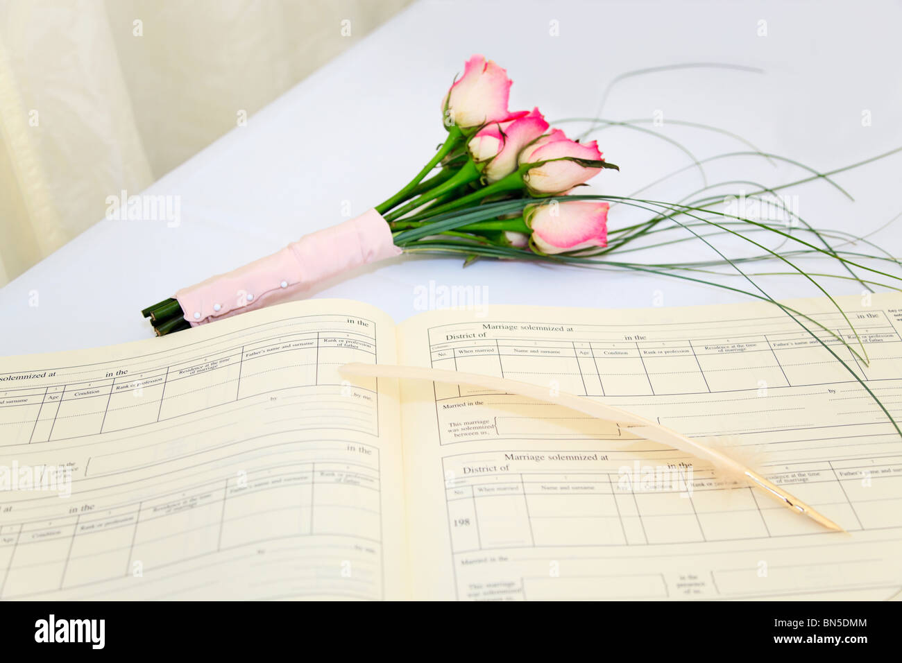 Un registro di matrimonio e il cappello con un bouquet di rose rosa su un tavolo bianco. Foto Stock