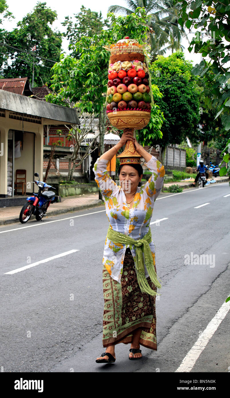 Donna Balinese a piedi lungo la strada che porta un tempio alto offrendo sul suo capo. Nei pressi di Ubud, Bali, Indonesia Foto Stock