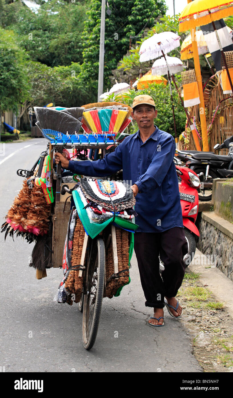 Uomo Balinese vendita di scope, stuoie e altri prodotti per uso domestico, dalla sua bicicletta. Questi uomini a piedi le loro biciclette intorno le strade Foto Stock