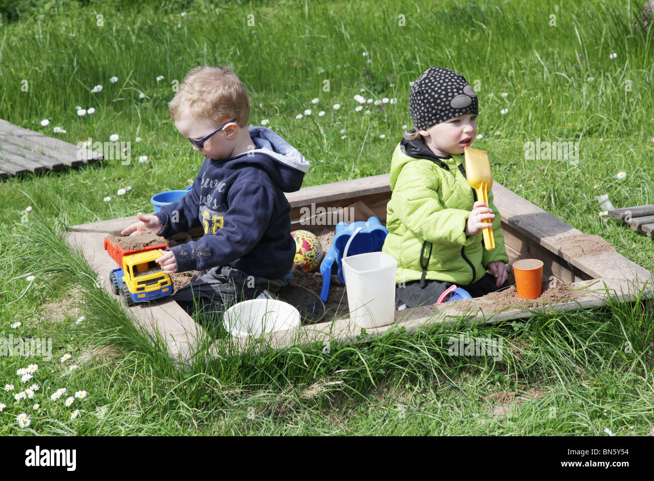 I bambini piccoli fratelli boy girl fratello la sorella in giardino a giocare in una buca di sabbia con giocattoli di plastica modello rilasciato Foto Stock