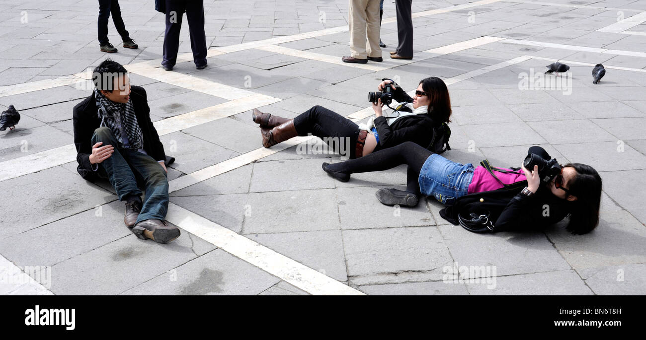 I giovani giapponesi turisti scattare foto in Piazza San Marco Venezia Italia. La posa sul pavimento per ottenere la giusta angolazione. Foto Stock