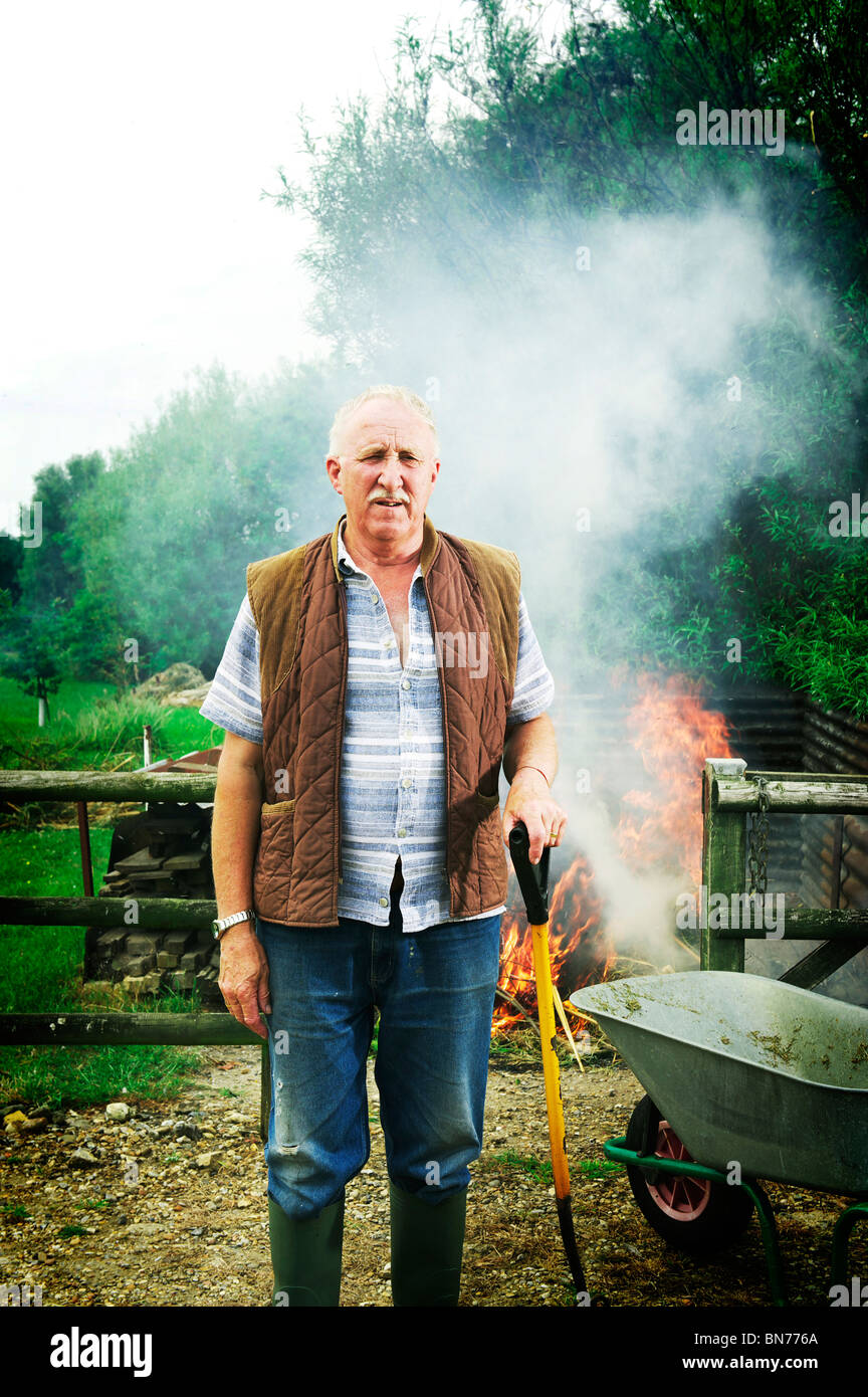 Il vecchio contadino maschio in campo con il fuoco rovente sul retro di lui Foto Stock