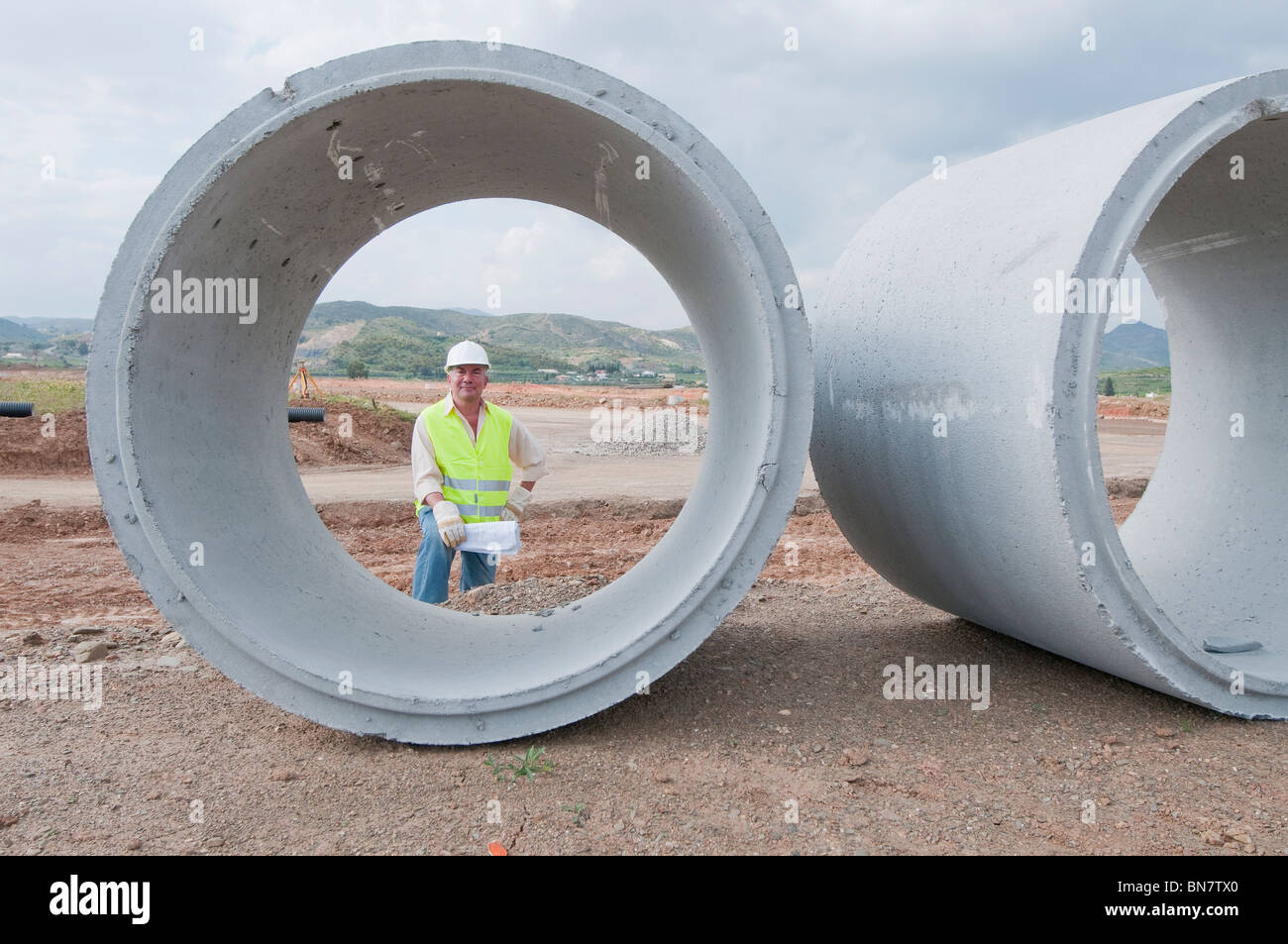 Lavoratore di ispanici in piedi vicino a grandi tubi di cemento Foto Stock