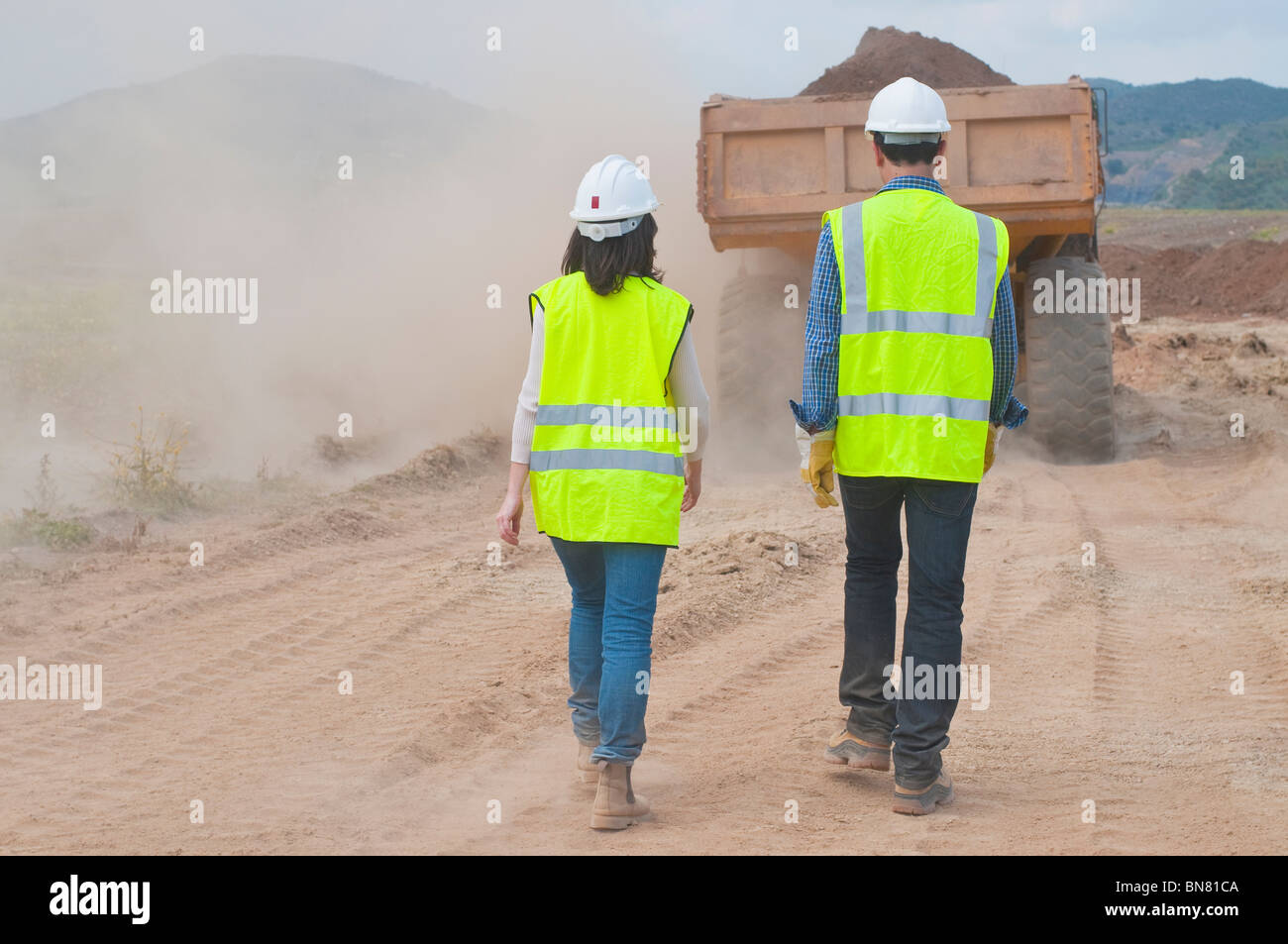 Lavoratori edili camminando dietro di autocarro con pianale di scarico Foto Stock
