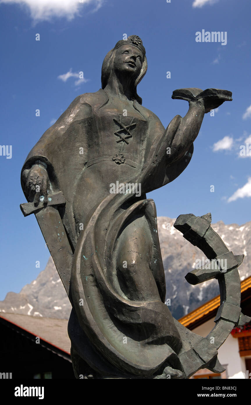 Statua di Saint Catharine sulla fontana del villaggio contro il massiccio Zugspitze, Lermoos, Tirolo, Austria Foto Stock