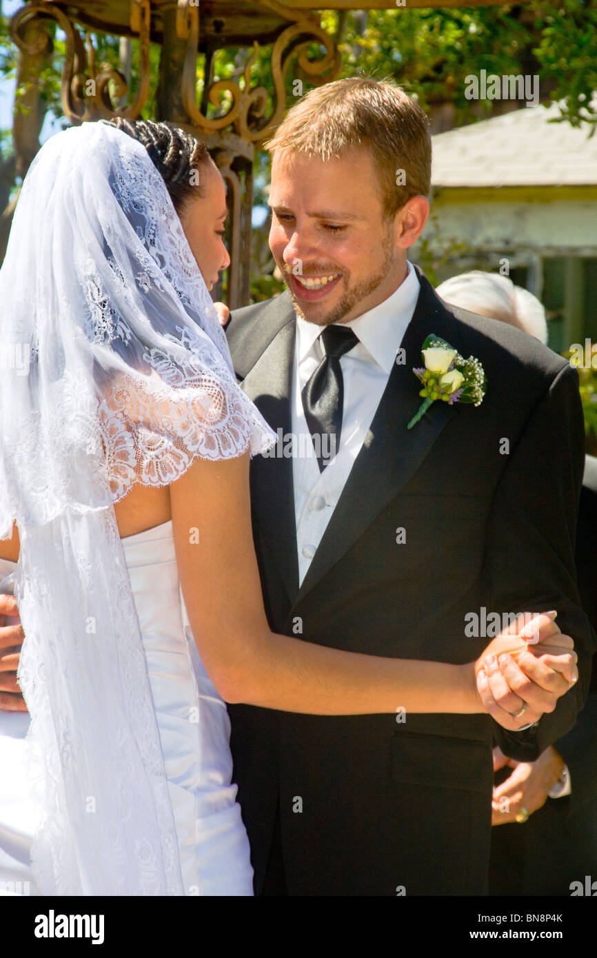 Un Caucasian sposo danze con il suo mixed-gara sposa a loro formale all'aperto la cerimonia di nozze in arancione, CA. Modello di rilascio Foto Stock
