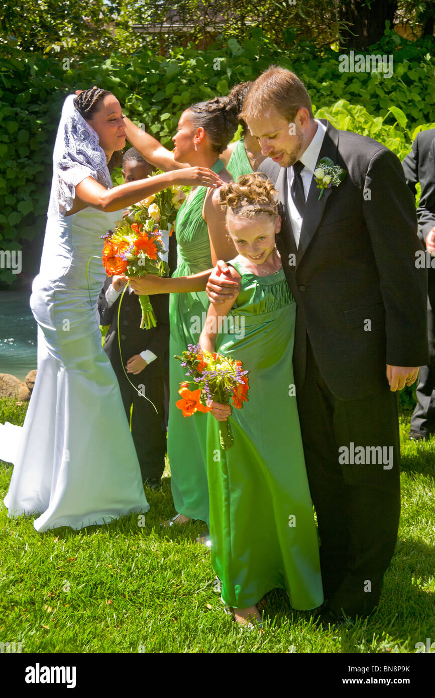 Un misto di gara sposa e Caucasico marito abbraccio loro bridesmaids dopo una formale all'aperto cerimonia di nozze, arancio, CA MODELLO DI RILASCIO Foto Stock