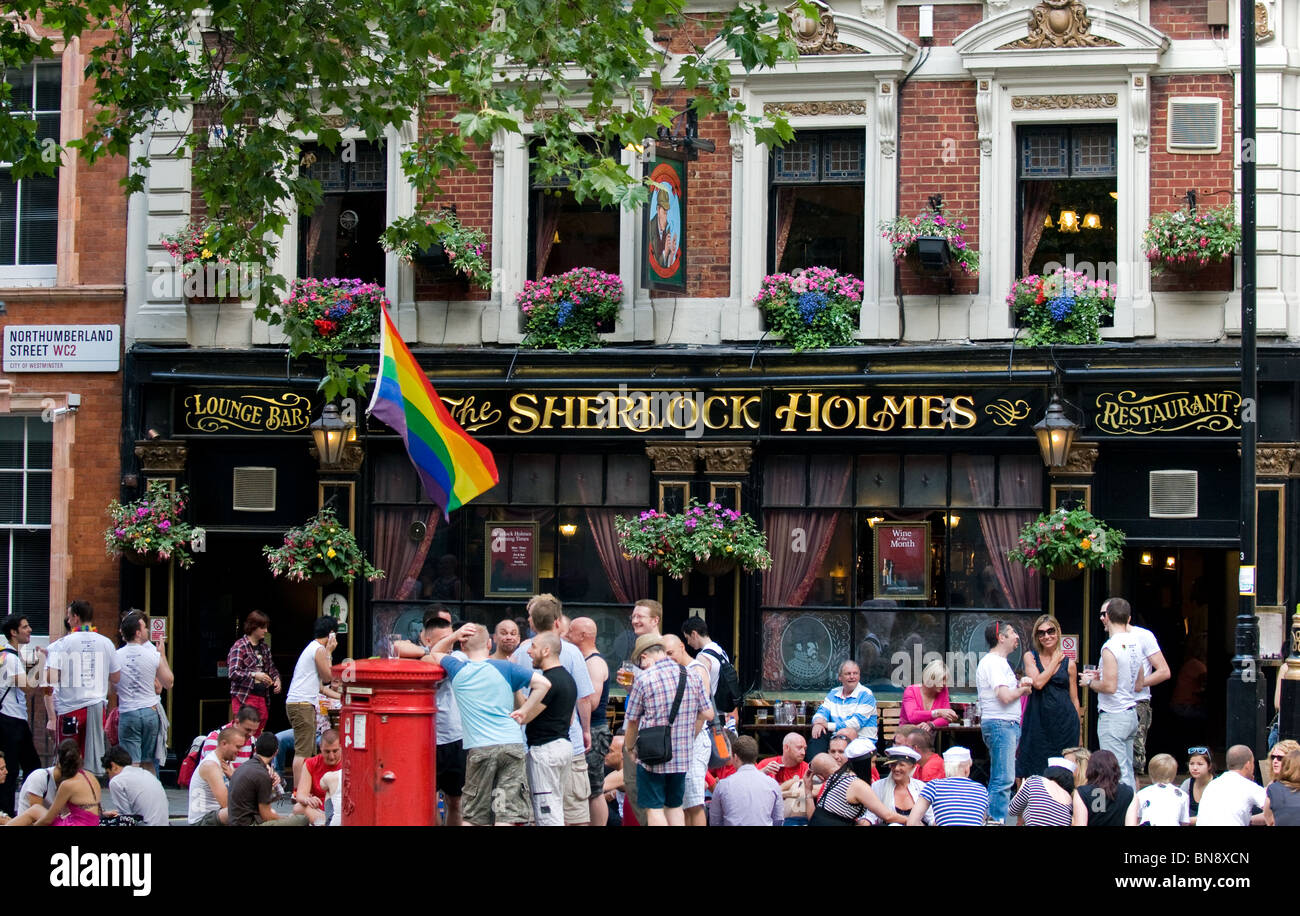Un Gay Pride bandiera e una folla di persone al di fuori del programma Sherlock Holmes Pub di Londra. Foto Stock