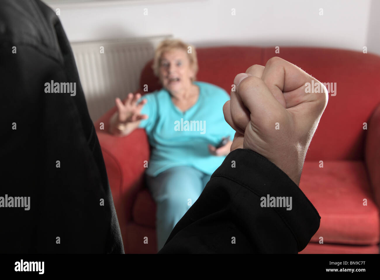 Maschio di pugno alzato volti verso un'anziana donna seduta su un divano a casa Foto Stock