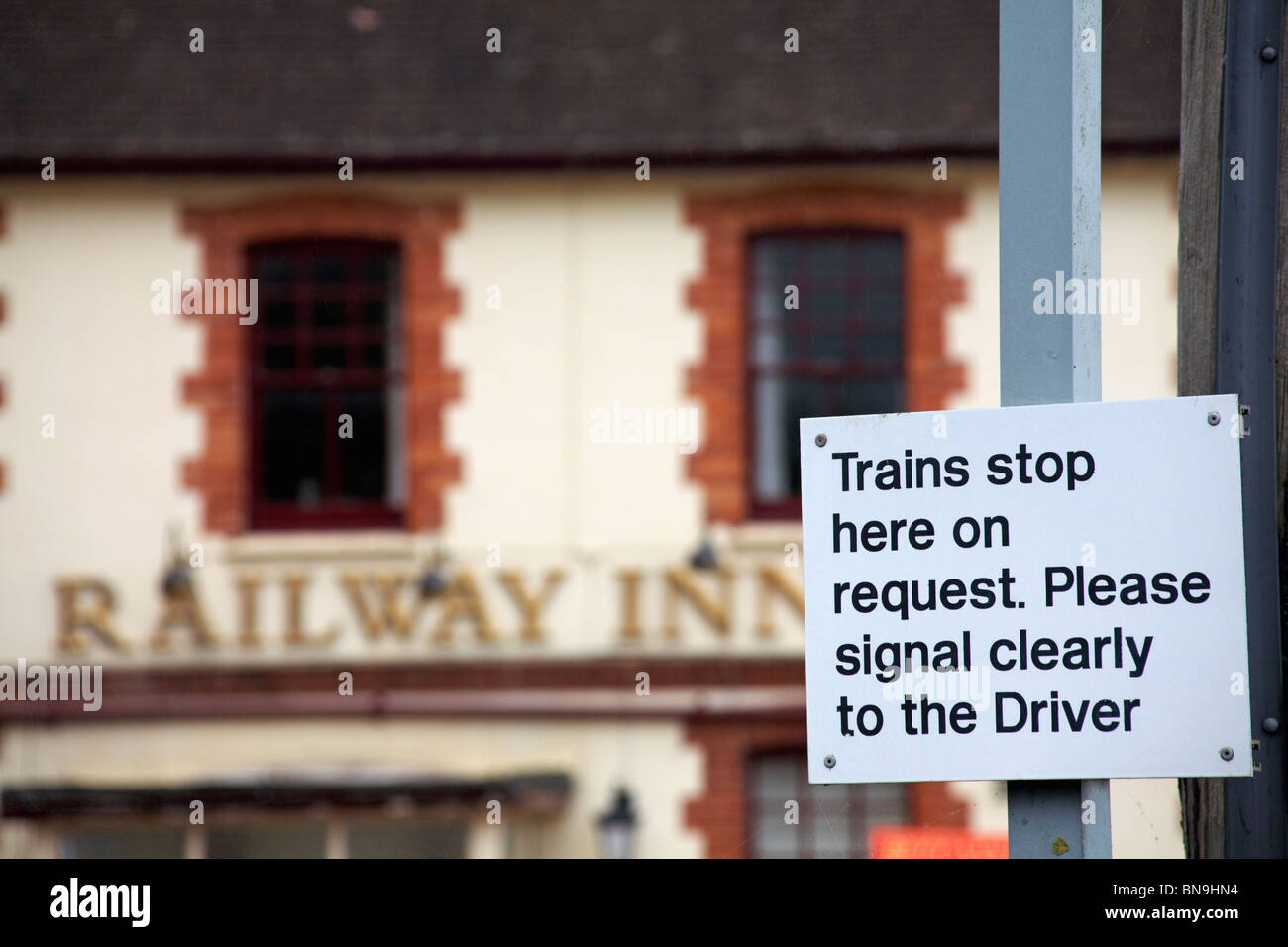 I treni diretti fermano qui su richiesta. Si prega di indicare chiaramente al conducente segno alla stazione Yetminster con fuori fuoco Railway Inn dietro Foto Stock