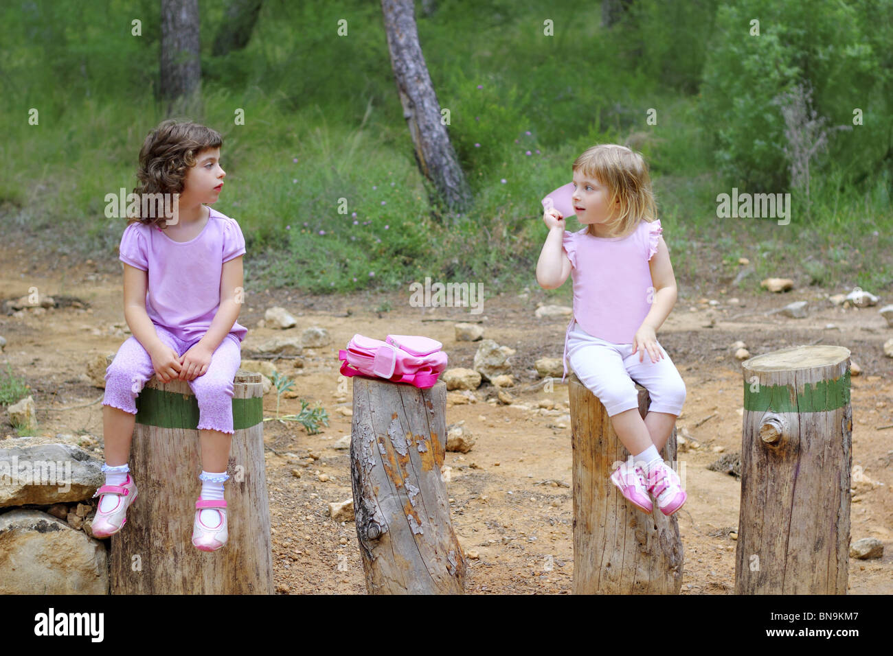 Due bambine sedersi sul parco foresta di tronchi di alberi verdi pinete Foto Stock