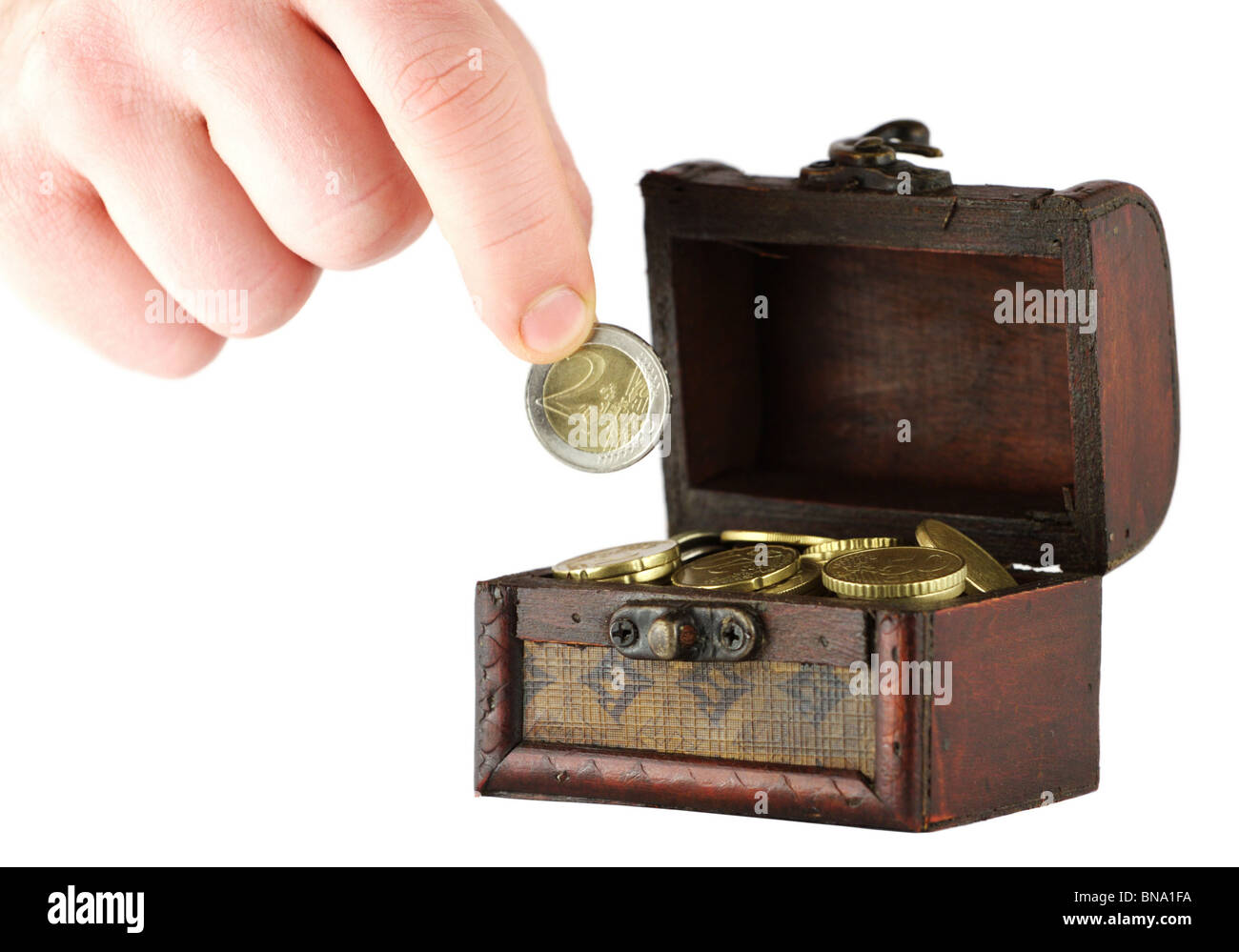 Vecchio scrigno pieno di monete e una mano che regge due euro e moneta Foto Stock